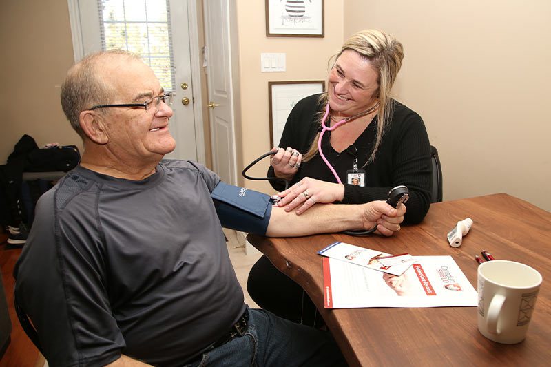 A nursing staff from Canadian Shield Health testing the blood pressure of an elderly man comfortably from his own home.