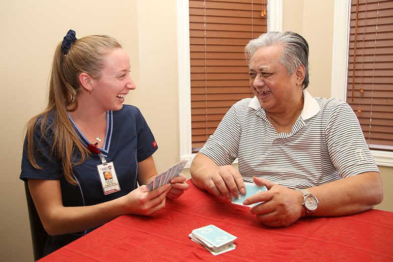 A private home care staff from Canadian Shield Health playing cards and having a good time with an elderly man at his home.