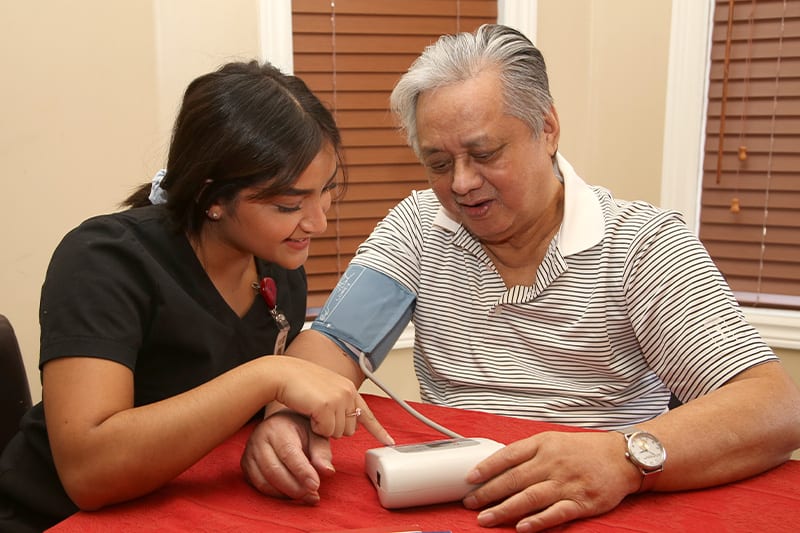A personal care staff from Canadian Shield Health showing a senior man, his own blood pressure results.